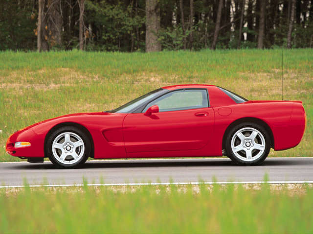 A 1999 Cherry Red Chevy Corvette parked on a road surrounded by grassy fields with a backdrop of trees in McGregor TX.